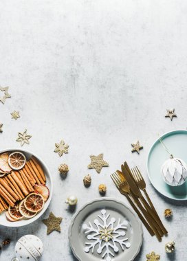 Christmas background with table setting, plates, golden cutlery, decoration and fir green, snow and cinnamon sticks, baubles at concrete backdrop. Festive dinner background. Top view. Copy space clipart