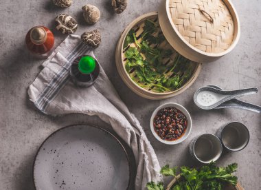 Asian food on grey concrete: shiitake mushrooms, steaming basket, hoisin sauce, coriander and spicy dip, empty plate and traditional crockery. Food background with ingredients and utensils. Top view. clipart