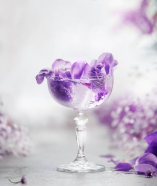 Açık gri masada mor çiçekli şampanya bardağı.
