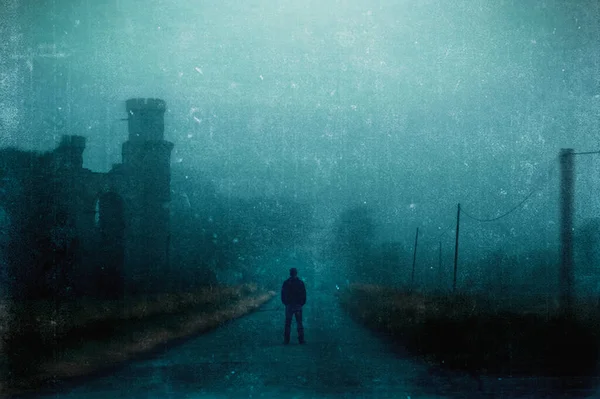 一个男人站在一个被废弃的废墟旁边的多雾的乡间道路上 用恐怖的咕噜声编辑 — 图库照片