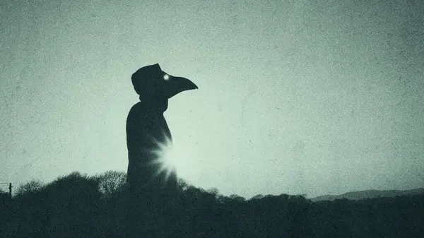 一个神秘的恐怖人物戴着瘟疫医生的乌鸦面具 冬天的时候 轮廓映衬在阳光下 用一个闷闷不乐的 肉麻的老式编辑 图库照片