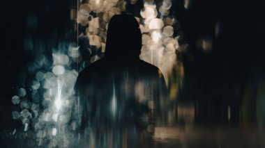 Ürkütücü, gizemli, kukuletalı bir şahsın iki kez teşhir edilmesi. Bokeh ve sokak lambalarıyla. Karanlık, kasvetli bir gecede