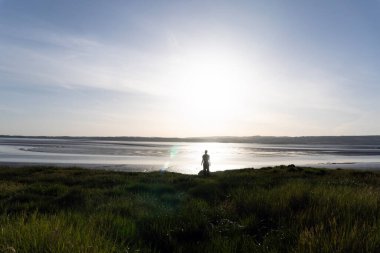Güneşin silueti altında kalmış bir adam. Yazın kırsal kesimde bir nehrin yanında duruyor.