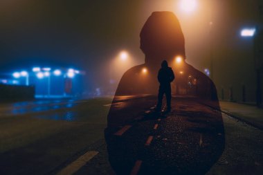 Kasvetli bir şehirde sisli bir gecede sokak ışıklarıyla siluetli gizemli bir kuletalı figür. Çift pozlama düzenleme ile