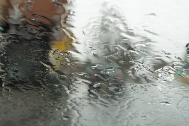 Arkaplanda şehir trafiği varken arabanın ön camındaki yağmurun yakın görüntüsü bulanıklaştı, İngiltere.