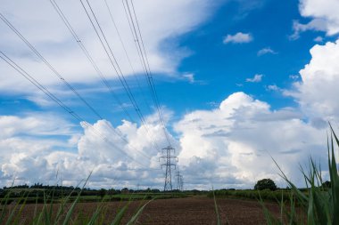 Kırsal kesimde bir elektrik direği hattı. Yazın mavi gökyüzü ve bulutlarla. İngiltere. Kopyalama alanı ile