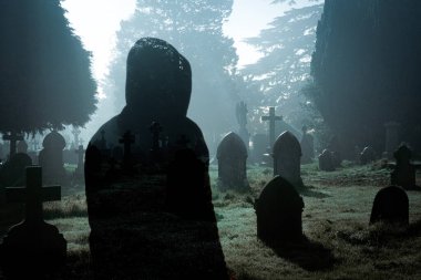 Çifte maruz kalma korku kurgusu. Ürkütücü sisli bir gecede mezarlıktaki kapüşonlu hayalet figürü