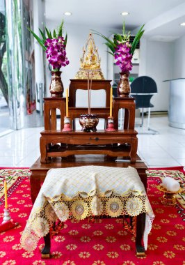 Meditasyon pozunda altın bir Buda heykeli, pırıl pırıl mücevherlerle süslenir ve küçük ahşap bir masaya yerleştirilir..