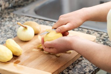 Evinin mutfağında patates soyan genç bir kadının yakın çekimi. Geleneksel İspanyol omleti hazırlama kavramı.