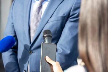 Basın konferansında elinde mikrofon ve akıllı telefon tutan gazeteci medya röportajı yapıyor