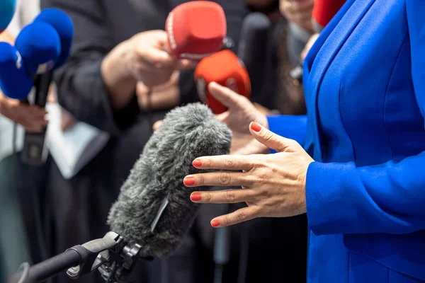 Journalist holding microphones making media interview with female politician or business woman