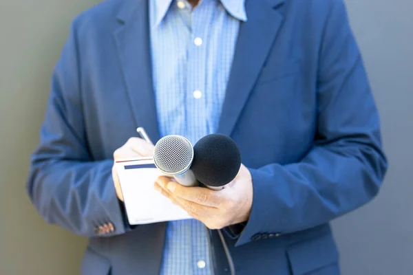 Reporter at media event or news conference, holding microphone, writing notes. Broadcast journalism concept.