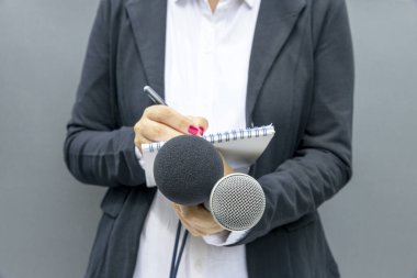 Basın konferansında kadın gazeteci, notlar yazıyor, mikrofon tutuyor.