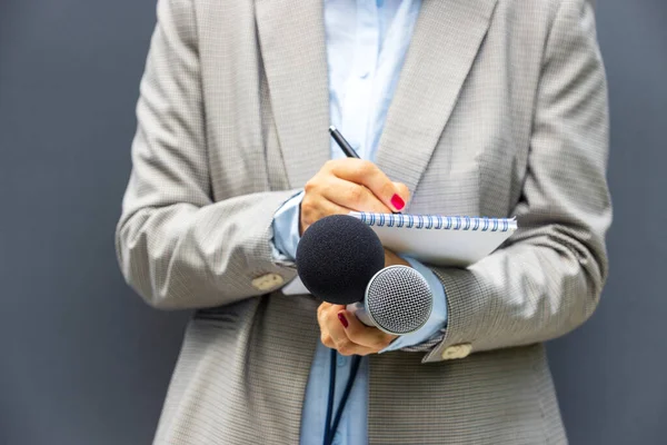 Journalist or reporter at media event, holding microphone, writing notes. Journalism concept.