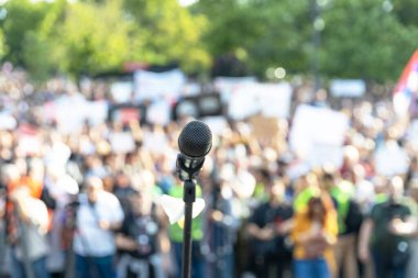 Mikrofona odaklan, arka planda kitlesel protestoda bulanık bir grup insan