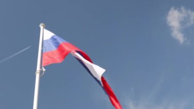Slovenya bayrağı rüzgarda dalgalanırken mavi gökyüzüne, uçak arkada iz bırakıyor