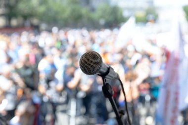 Açık hava etkinliklerinde bulanık bir kalabalık tarafından çevrelenmiş, odak noktasında bir mikrofonun yakın plan görüntüsü.