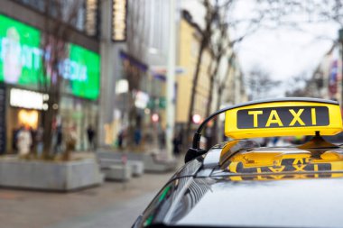Dükkanlar, binalar ve yayalarla çevrili hareketli bir şehir caddesine park etmiş parlak sarı bir taksi.