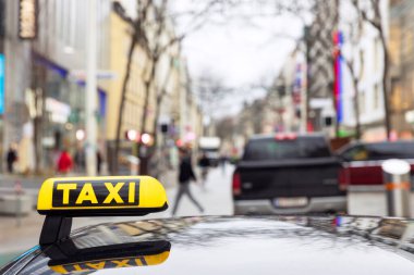 Şehir merkezinde bulutlu bir caddede araçları ve yayaları olan bir şehir caddesine odaklanan taksi tabelası.