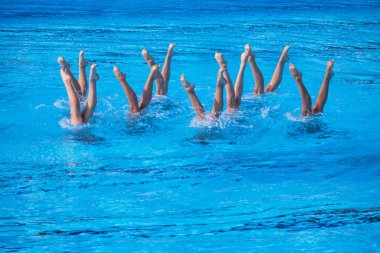 Senkronize veya sanatsal yüzücüler zarif ve hassas bir su rutini uyguluyorlar. Bacakları zarif bir şekilde havuzda.