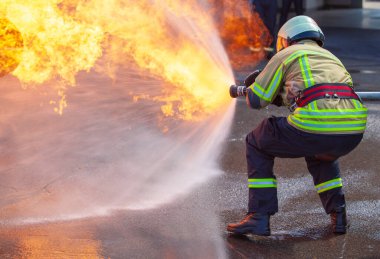 Koruyucu giysili bir itfaiyeci, acil bir durumda büyük yangınları kontrol etmek ve söndürmek için hortumdan su püskürtüyor.