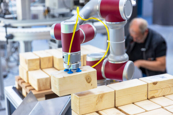 Collaborative industrial robot arm operating alongside blurred human worker while stacking wooden blocks in a smart factory environment