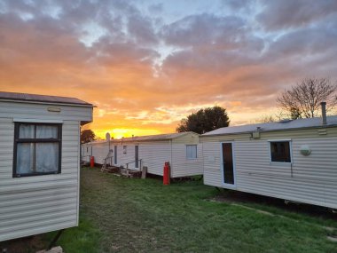 Hareketli bir günbatımı gökyüzü altında huzurlu ve huzurlu kırsal bir manzarayı aydınlatan hareketli evler. Tatil, dinlenme ve açık havada yaşama kavramları için ideal..