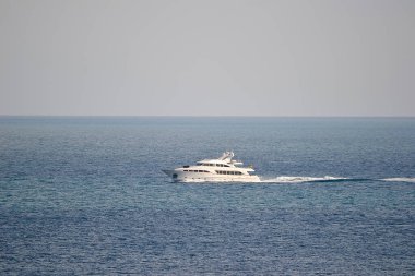 Beyaz bir yat sakin mavi okyanusta yol alır ve ardında hafif bir iz bırakır. Sahne sakin, temiz bir gökyüzünün altında görünen başka bir gemi ya da kara yok..