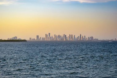 Kolombiya, Cartagena 'nın ufuk çizgisi, altın gün batımına karşı modern yüksek binalara ev sahipliği yapıyor. Ön plandaki sakin sular sakin sahneyi güçlendirir..