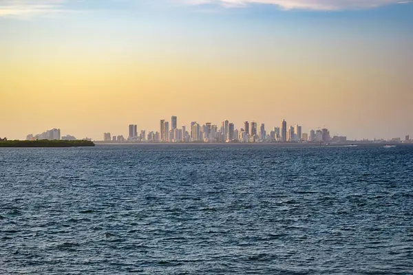 Kolombiya, Cartagena 'nın ufuk çizgisi, altın gün batımına karşı modern yüksek binalara ev sahipliği yapıyor. Ön plandaki sakin sular sakin sahneyi güçlendirir..