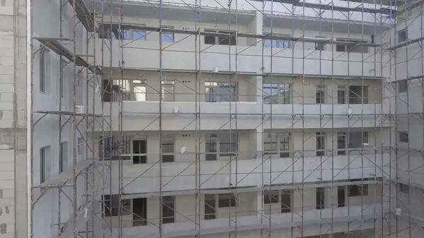 Geniş bir iskeleye sahip modern bir çok katlı bina yapım aşamasında. Yapıda, kentsel bir alanda tek tip balkonlar ve büyük pencereler yer alıyor..