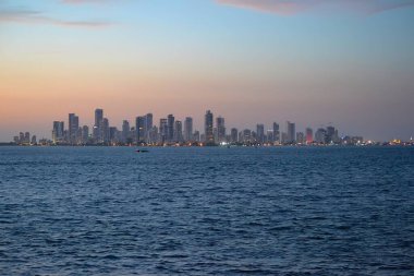 Alacakaranlıkta Kolombiya 'nın ufuk çizgisi olan Cartagena' da, turuncu ve mavi gökyüzüne karşı modern gökdelenler yer alırken, ön planda Karayip Denizi yer alıyor..