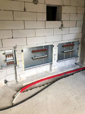 Bitmemiş beton zeminde, borular, kırmızı vanalar ve su tesisatı için metal panelleri olan bir inşaat alanının iç görüntüsü..