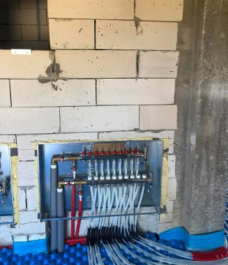 İnşaat duvarında kırmızı ve beyaz borularla korunmasız tesisat ve ısıtma sistemleri bulunuyor. Zemin mavi bir koruyucu katmanla kaplı..