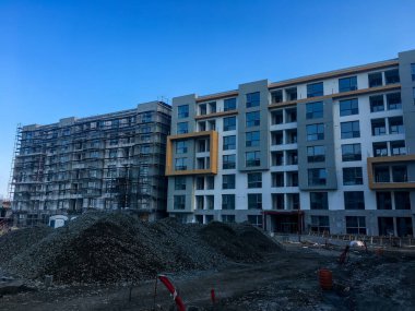 Açık mavi bir gökyüzünün altında, bir binanın iskelesi ve sarı pencere çerçeveleri olan neredeyse tamamlanmış bir yapıya sahip aktif inşaat alanı..