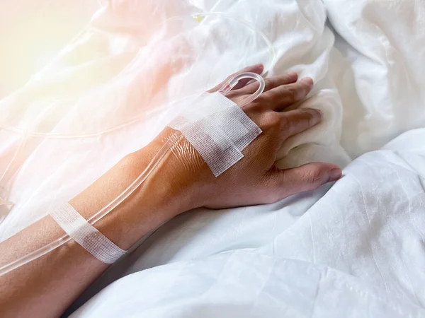 stock image patient on hospital bed with blurry of Saline intravenous (iv) drip on hand in hospital, Needles and saline tubes are punctured on the patient's hand, Health care and Medical equipment concept.