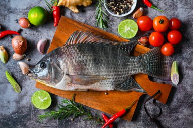 Tilapia baharatlı biberiyeli biberiye limonlu zencefilli sarımsaklı biber koyu arkaplanda, Tilapia çiftliğinden taze çiğ tilapia balığı.