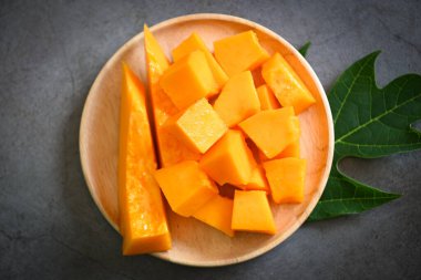 Papaya meyveleri koyu arkaplanda, taze olgun papaya dilimleri tabakta tropikal meyveler ve papaya yaprakları - üst manzara