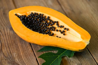 Papaya tohumu ve papaya yaprağı yapraklarıyla taze olgun papaya tropikal meyvesi, ahşap arka planda papaya meyveleri.