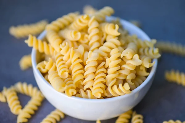 Raw pasta macaroni on white bowl, close up raw macaroni spiral pasta uncooked delicious fusilli pasta for cooking food