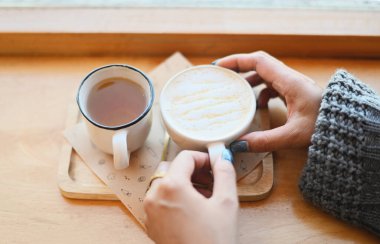 coffee caramel and tea - woman coffee with hand holding a cup on the wood table, caramel coffee cup in the cafe morning, hot caramel macchiato in the winter - top view 