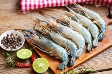 fresh shrimps prawns seafood shelfish with herb and spices chilli pepper lemon lime rosemary, raw shrimp on plate background for cooking food - top view