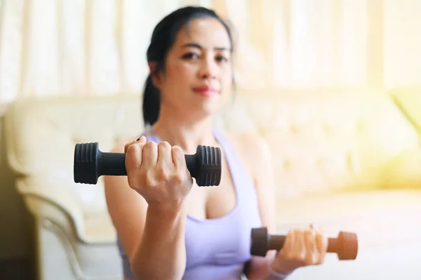 sporty woman exercise muscles in sportswear with dumbbell at home in the living room, woman exercising at home, woman dumbbells in her hands, sport recreation health care concept