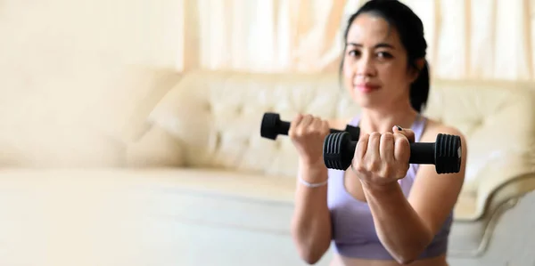 sporty woman exercise muscles in sportswear with dumbbell at home in the living room, woman exercising at home, woman dumbbells in her hands, sport recreation health care concept