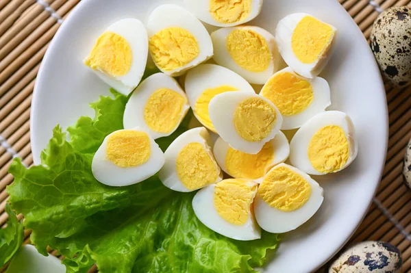 boiled eggs food, quail eggs on white plate, breakfast eggs with fresh quail eggs and vegetable lettuce salad on wooden table background - top view