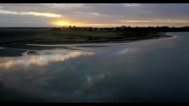 Güzel, sakin bir günbatımı manzarası, sakin bir nehre nazikçe yansıyor, nazik kıyılarla çevrili.