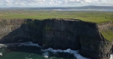 Bulutlu ve kasvetli bir gökyüzünün altında okyanusla buluşan dramatik uçurumları gösteren nefes kesici bir hava manzarasının tadını çıkar.