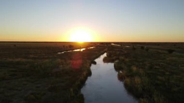 Büyüleyici güzellikte bir gün batımı göz kamaştırıcı bir şekilde geniş çayırlara kurulmuş sakin ve sakin bir su yolunu aydınlatıyor.