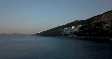 Güzel, sakin bir kıyı manzarası. Hafif dalgalar ve akşam gökyüzünün altındaki tepeler.