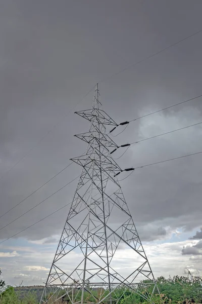 High voltage electric line tower with dark monsoon cloud background.